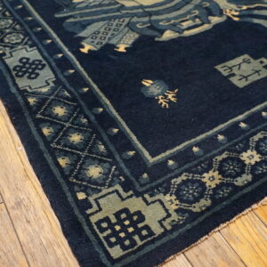 Navy rug with elaborate blue and yellow traditional patterns rests on distressed wood flooring.