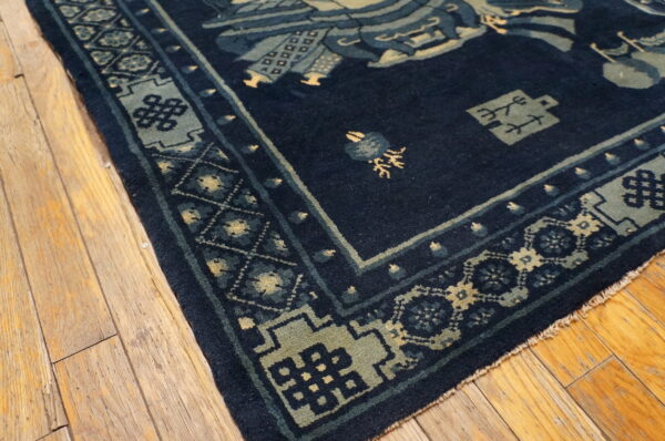Navy rug with elaborate blue and yellow traditional patterns rests on distressed wood flooring.
