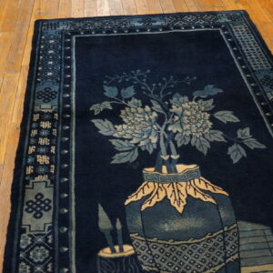 Dark blue rug with light blue and beige flowers in a vase design, bordered, resting on wood planks.