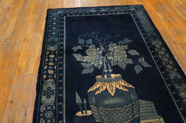 Dark blue rug with light blue and beige flowers in a vase design, bordered, resting on wood planks.