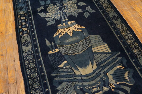 Dark blue rug with pale blue and tan floral and geometric motifs lying on a wood floor.