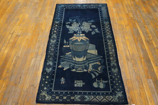 Dark blue runner rug featuring a vase of flowers and symbolic objects, displayed on distressed wood floors.