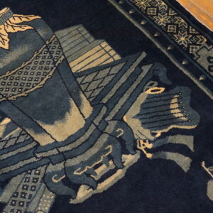 Detail of a dark blue rug featuring complex designs in muted green and pale yellow tones near wood flooring.