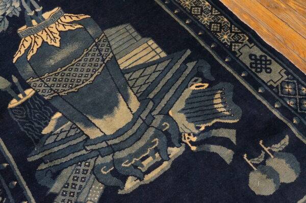 Detail of a dark blue rug featuring complex designs in muted green and pale yellow tones near wood flooring.