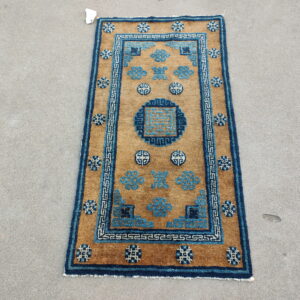 Tan field rug featuring geometric blue motifs and a key border pattern on gray concrete.
