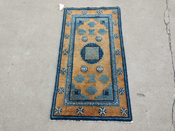 Tan field rug featuring geometric blue motifs and a key border pattern on gray concrete.