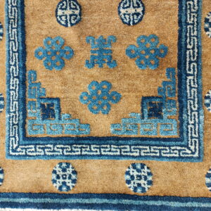 High-pile rug in tan with dark blue and light blue stepped borders and geometric field motifs.