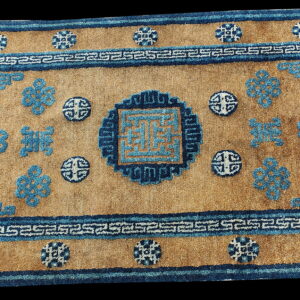 Medium pile rug displays a golden-tan field with geometric borders and intricate blue symbolic designs.