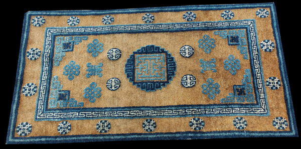 Medium pile rug displays a golden-tan field with geometric borders and intricate blue symbolic designs.