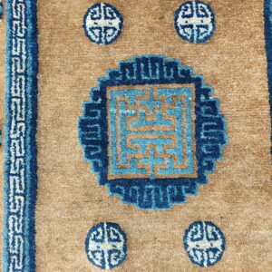 Detail of a high-pile tan rug featuring dark and light blue key patterns and circular medallions.