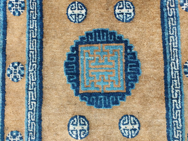 Detail of a high-pile tan rug featuring dark and light blue key patterns and circular medallions.