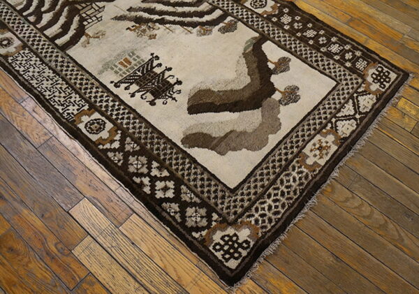Textured brown and cream rug with geometric borders and stylized figures rests on rustic wood flooring.