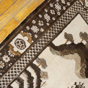 Cream and dark brown rug featuring stylized geometric and tree motifs resting on rustic wood planks.