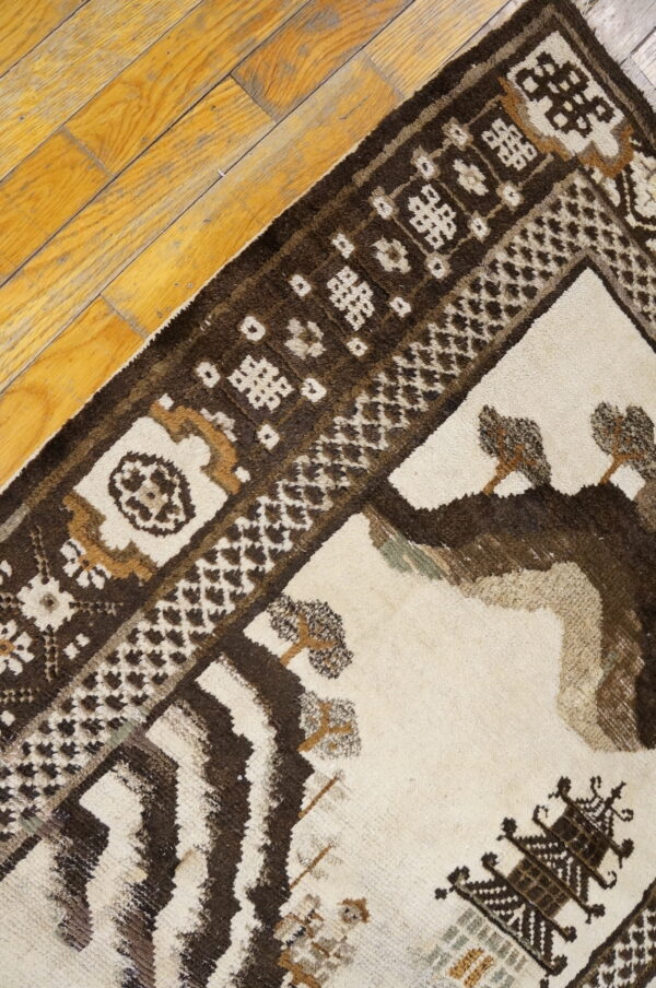 Cream and dark brown rug featuring stylized geometric and tree motifs resting on rustic wood planks.