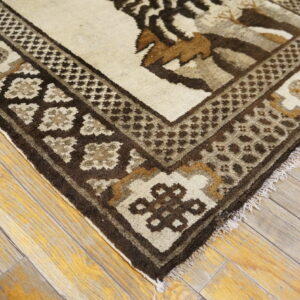 Geometric patterned rug in shades of brown and cream rests on distressed, light-toned wooden floorboards.