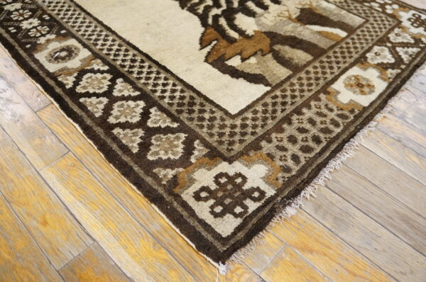 Geometric patterned rug in shades of brown and cream rests on distressed, light-toned wooden floorboards.