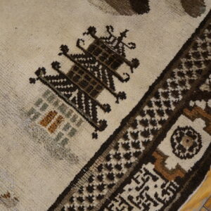 Medium-pile rug detail showing cream and dark brown geometric designs with small sage and rust accents on a wood floor.