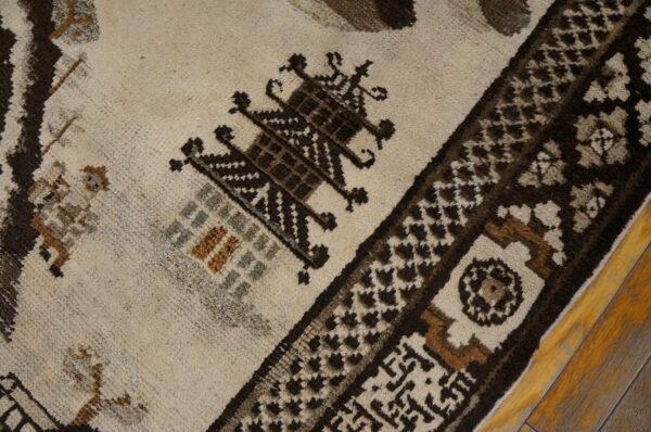 Medium-pile rug detail showing cream and dark brown geometric designs with small sage and rust accents on a wood floor.