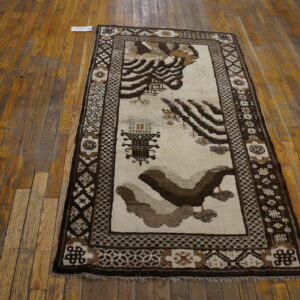 Runner rug with abstract brown and cream motifs and geometric borders on distressed wood flooring.