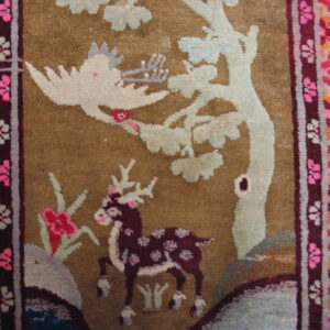 Plush rug detail showing a spotted deer and bird motif on an olive-tan field with geometric bright red borders.