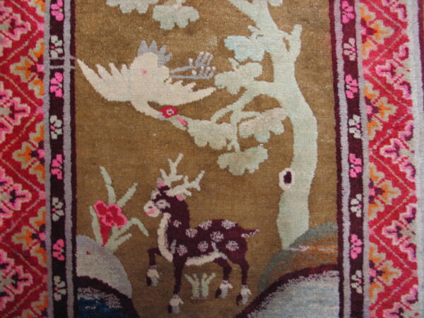 Plush rug detail showing a spotted deer and bird motif on an olive-tan field with geometric bright red borders.