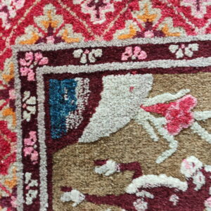 Highly textured rug corner featuring complex traditional motifs in red, tan, maroon, pink, and bright blue.
