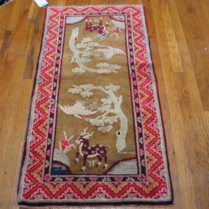 A brown, low-pile runner featuring white cranes and a maroon deer, surrounded by a vivid red and pink border.