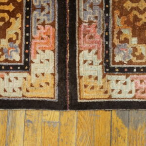 Brown and gold patterned rug border with pink and blue accents lies on distressed wooden floorboards.