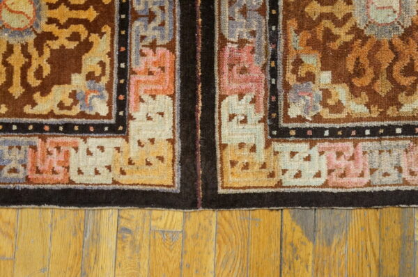Brown and gold patterned rug border with pink and blue accents lies on distressed wooden floorboards.
