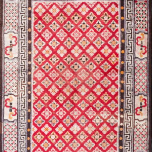 Red rug with repeating white floral diamonds, framed by dark brown and Greek key patterned borders.