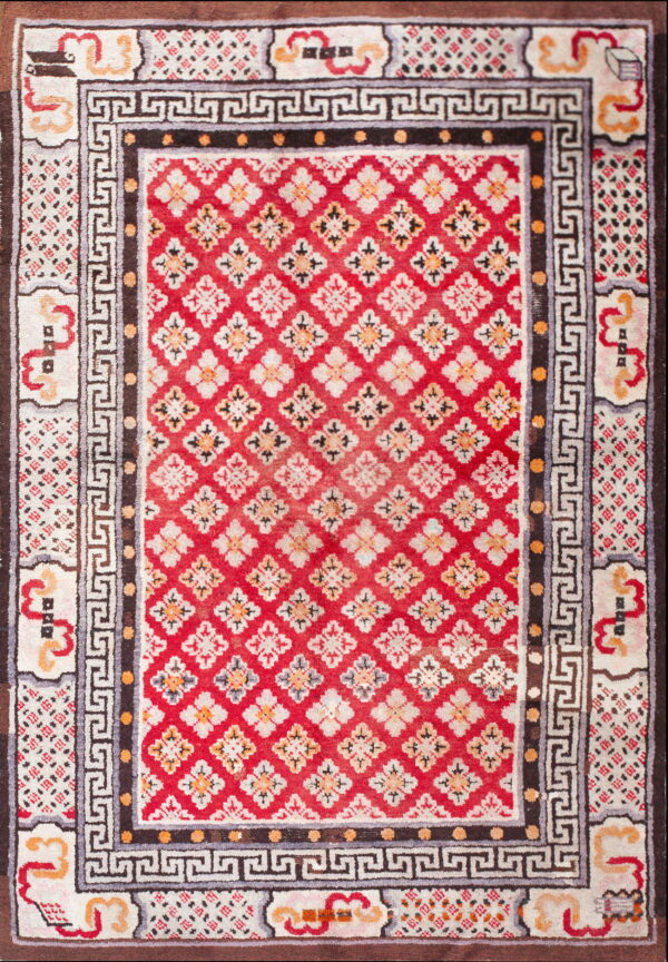 Red rug with repeating white floral diamonds, framed by dark brown and greek key patterned borders.