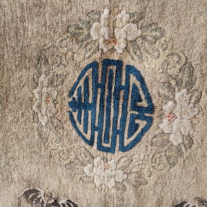Muted tan rug detail showing a bright blue octagonal symbol framed by white floral wreath motifs.