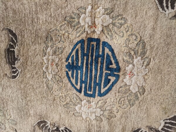 Muted tan rug detail showing a bright blue octagonal symbol framed by white floral wreath motifs.