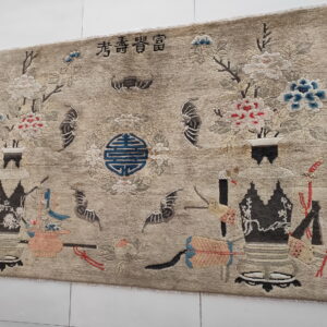 A beige rug with a pictorial pattern of vases, colorful flowers, bats, and script characters.