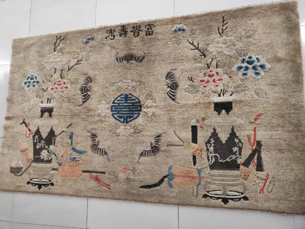 A beige rug with a pictorial pattern of vases, colorful flowers, bats, and script characters.