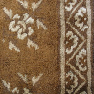 Textured brown rug with cream floral motifs and a patterned border lying on light wood planks.