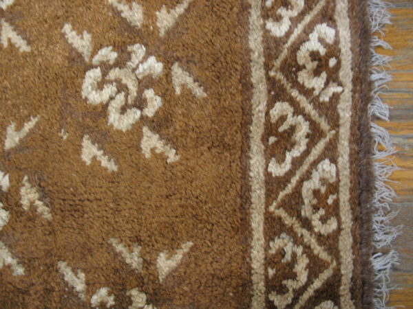 Textured brown rug with cream floral motifs and a patterned border lying on light wood planks.