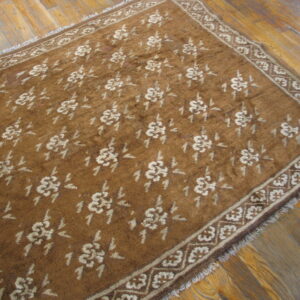 A low-pile brown rug featuring a repeating tan floral design and geometric border rests on plank hardwood flooring.