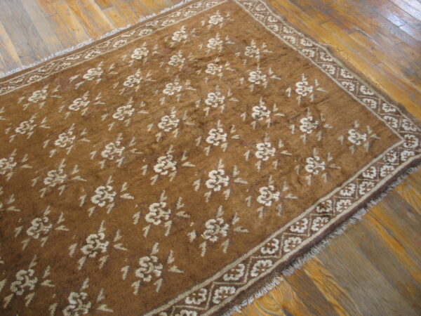 A low-pile brown rug featuring a repeating tan floral design and geometric border rests on plank hardwood flooring.