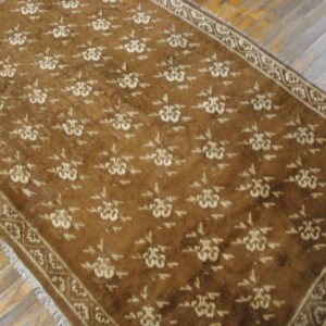 Brown and beige floral patterned rug with visible fringe covers rustic diagonal wood plank flooring.