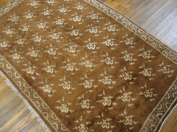 Brown and beige floral patterned rug with visible fringe covers rustic diagonal wood plank flooring.