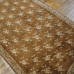 Brown rug featuring a repeating light floral design and fringed edges on a wood plank floor.