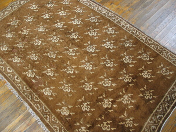 Brown rug featuring a repeating light floral design and fringed edges on a wood plank floor.