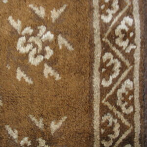 Brown high-pile rug detail shows light floral motifs and a geometric border resting on wood flooring.