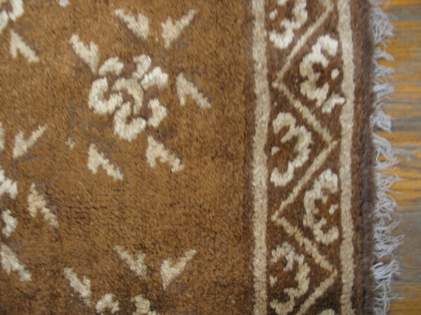 Brown high-pile rug detail shows light floral motifs and a geometric border resting on wood flooring.