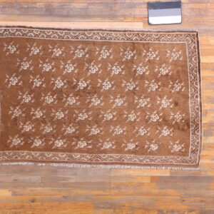 Low-pile brown rug with repeating light-toned floral pattern and border on wide wood planks.