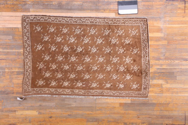 Low-pile brown rug with repeating light-toned floral pattern and border on wide wood planks.