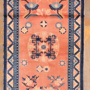 Narrow coral runner rug with elaborate navy blue medallions and geometric borders on plank wood flooring.