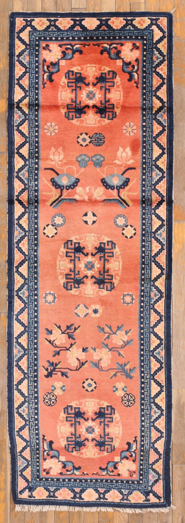 Narrow coral runner rug with elaborate navy blue medallions and geometric borders on plank wood flooring.