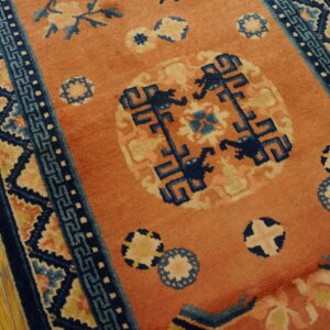 Coral rug with navy and light blue geometric borders and medallions rests on worn wood flooring.